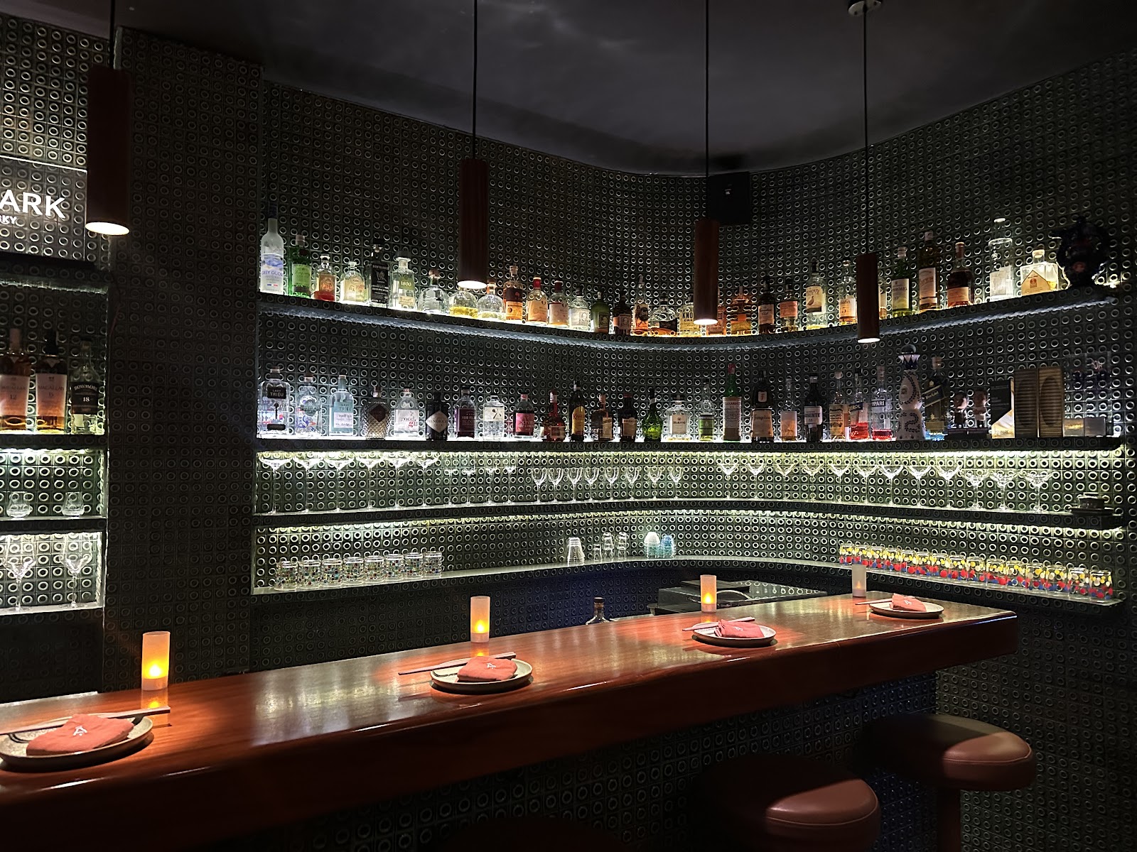 The bar with backlit bottle shelves, patterned tile and copper pendants
