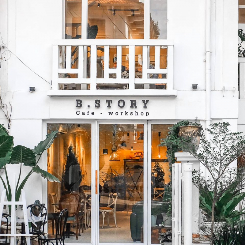 Tầng trệt ấm đèn — ghế mây, ghế nệm xanh, cửa kính lớn