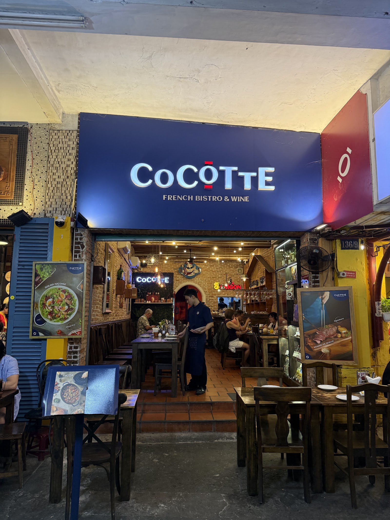 입구 위 파란 'COCOTTE FRENCH BISTRO & WINE' 간판, 옆에는 살라드 니수아즈와 로스비프 드 뵈프 포스터