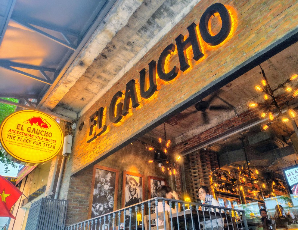 Tấm biển vàng "EL GAUCHO — ARGENTINIAN STEAKHOUSE — THE PLACE FOR STEAK" ngoài vỉa hè