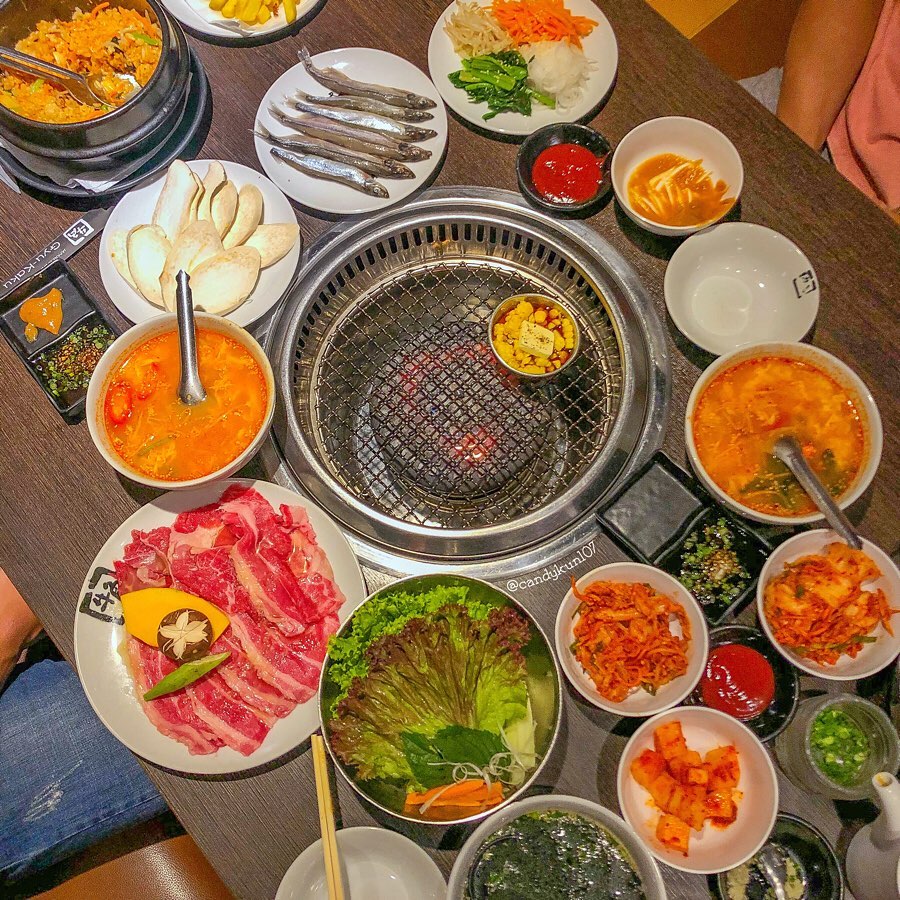 Bàn yakiniku từ trên cao: bếp than đỏ lửa, dĩa thịt bò sống, đồ ăn kèm