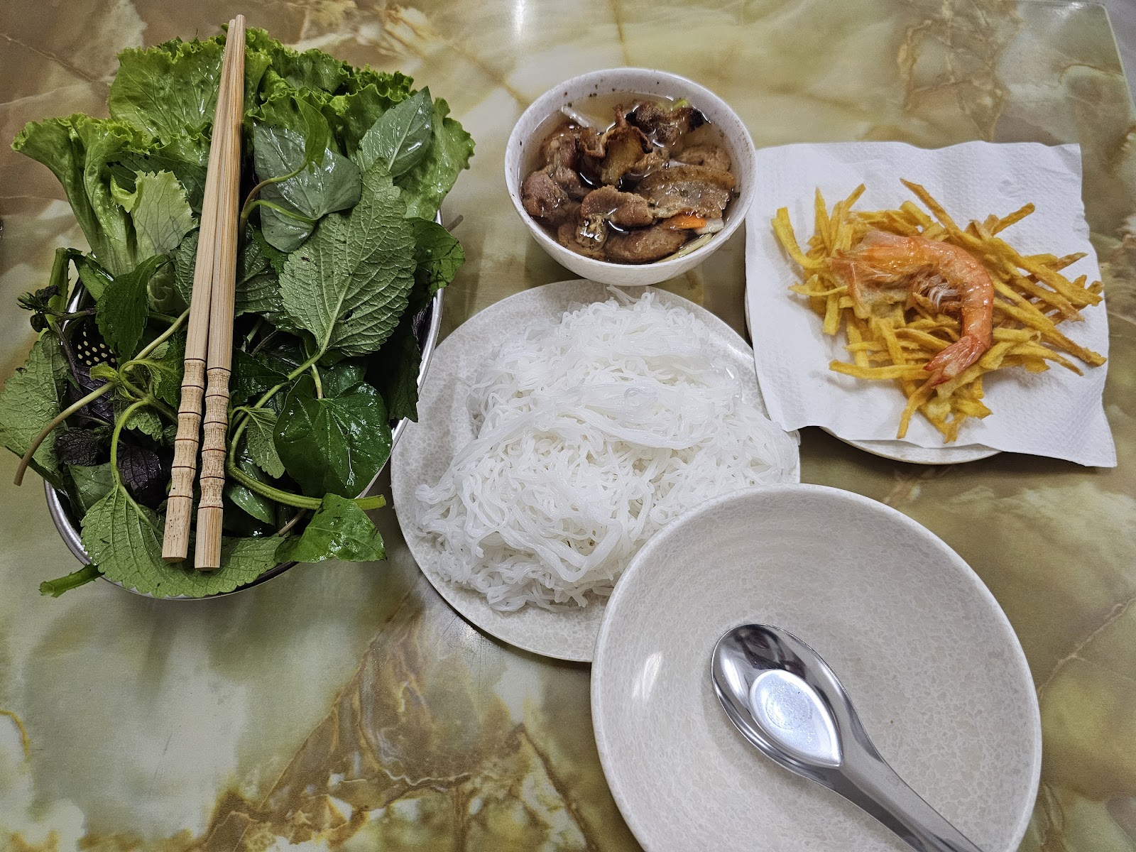 Phần bún chả đầy đủ — bát thịt nướng trong nước chấm, bún trắng, rau sống, đũa tre và món rán giòn