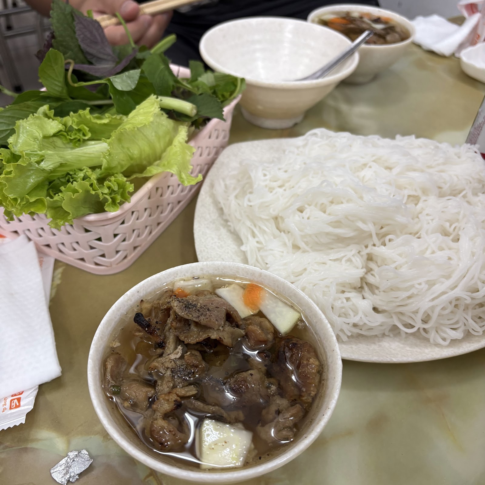 Cận cảnh bún chả — thịt nướng và chả viên trong bát nước chấm với dưa góp cà rốt, củ cải