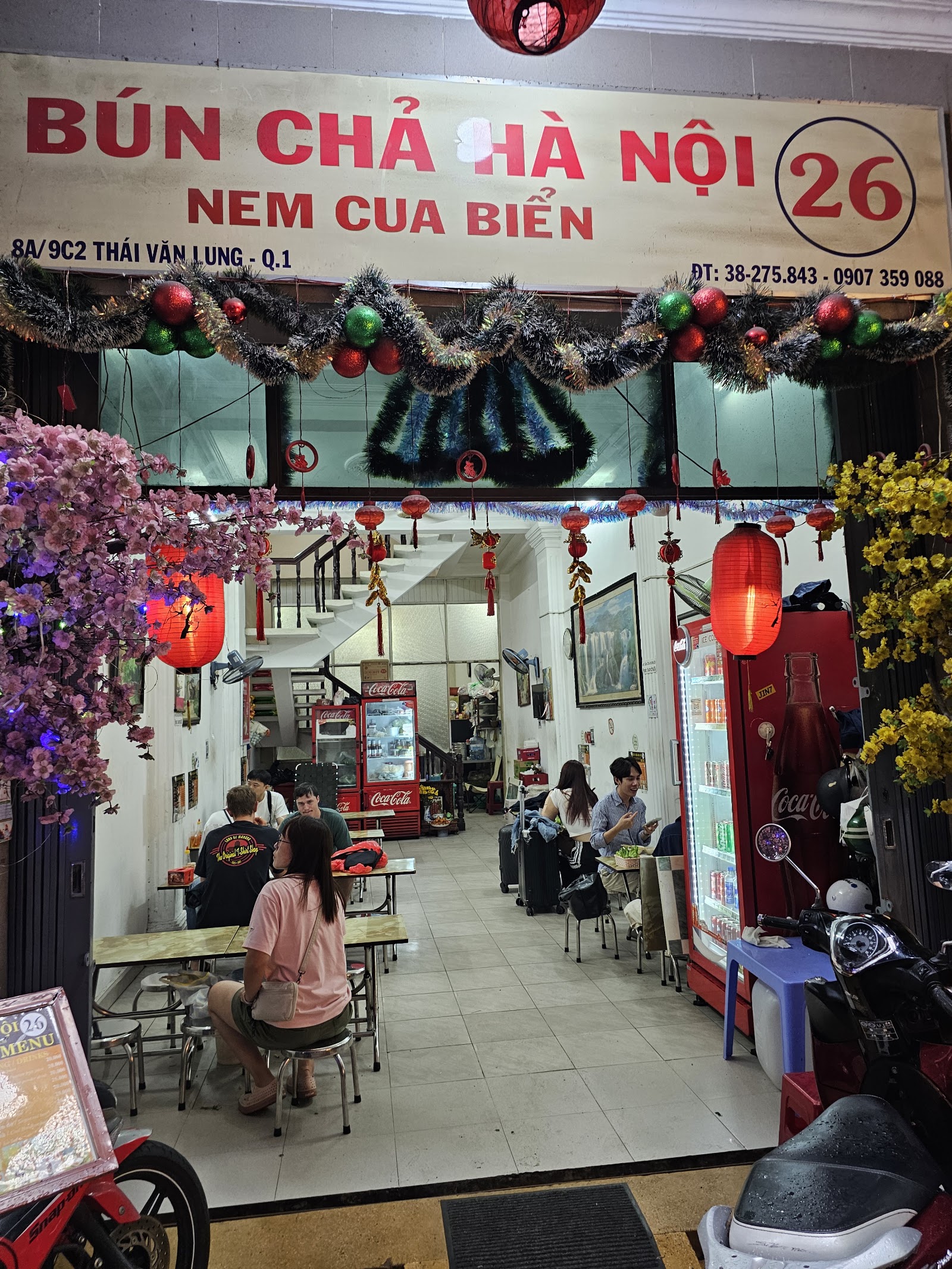 Mặt tiền quán buổi tối — biển hiệu chữ đỏ BÚN CHẢ HÀ NỘI 26, đèn lồng đỏ và cây đào