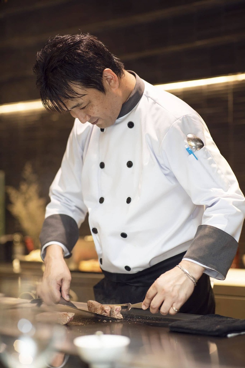 Đầu bếp xắt thịt bò trên bàn teppan
