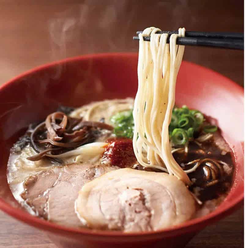 The signature red IPPUDO bowl — tonkotsu broth, chashu, black garlic oil, noodles lifted through steam