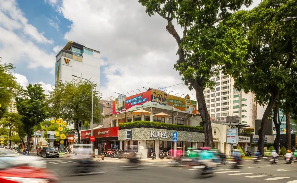 The Kafa Café facade on the Nguyen Thi Minh Khai x Pasteur crossroads — white KAFA letters on washed-stone walls, bright billboard above