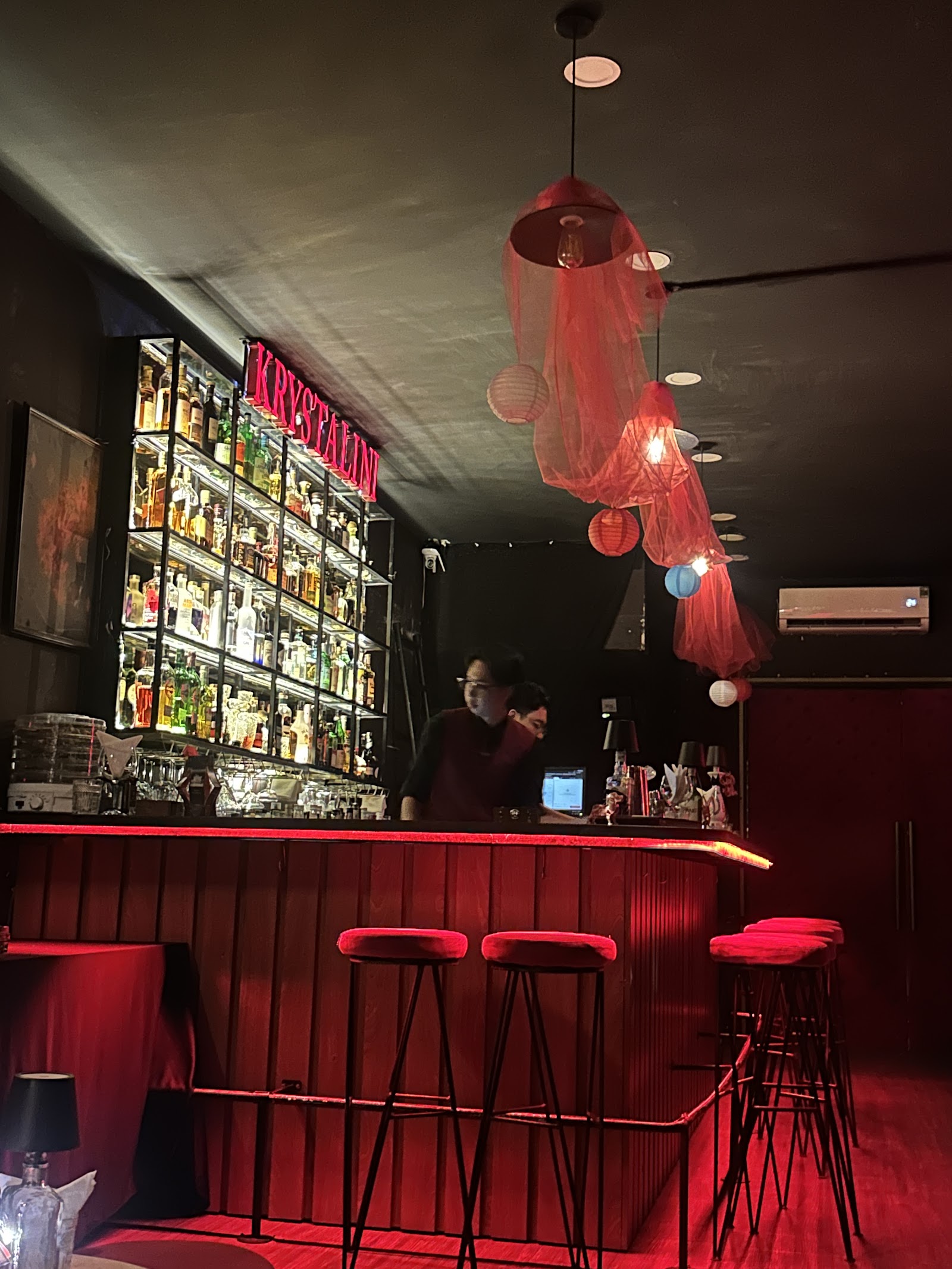 The bar counter with bartender under red fabric pendants