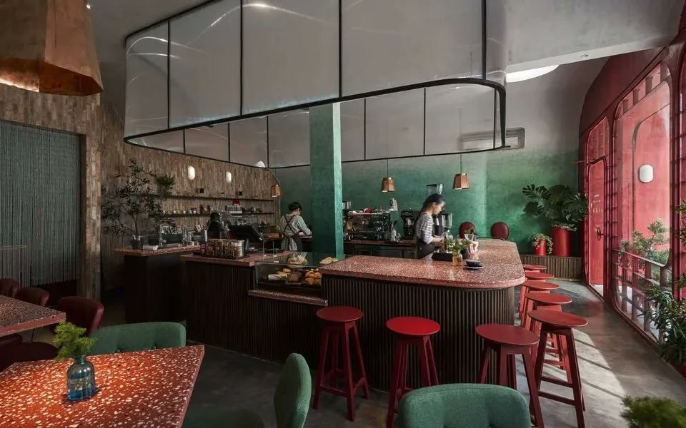 Chi nhánh «Tự Do»: quầy bar tròn đá mài đỏ giữa căn phòng vòm gạch nung, men xanh và đèn đồng. «Kindness in every cup.»