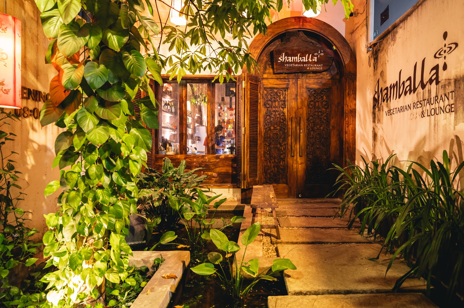 Shamballa's entrance by day — carved wooden doors under the sign, stone path through the garden