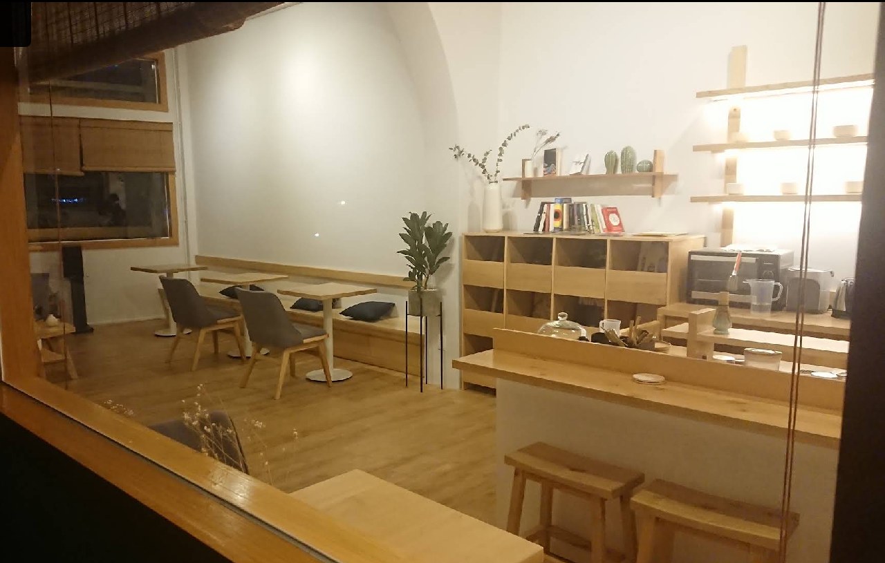 시부이 컨셉의 메인 룸 — 원목 테이블, 회청색 패브릭 의자, 불 켜진 도자기 선반