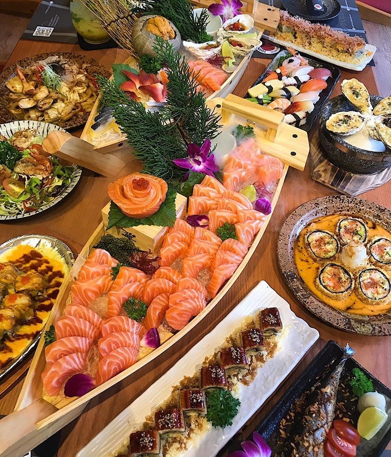 Wooden boat piled with salmon sashimi, a salmon rose and table dishes